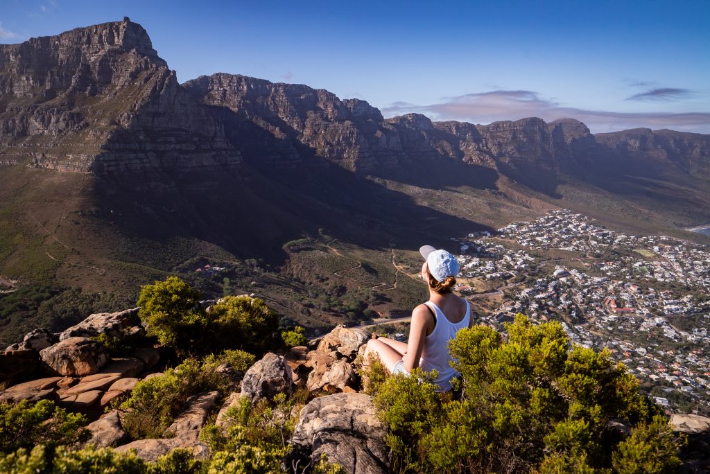 mulher irreconhecível sentada à beira de um penhasco a admirar a Cidade do Cabo
